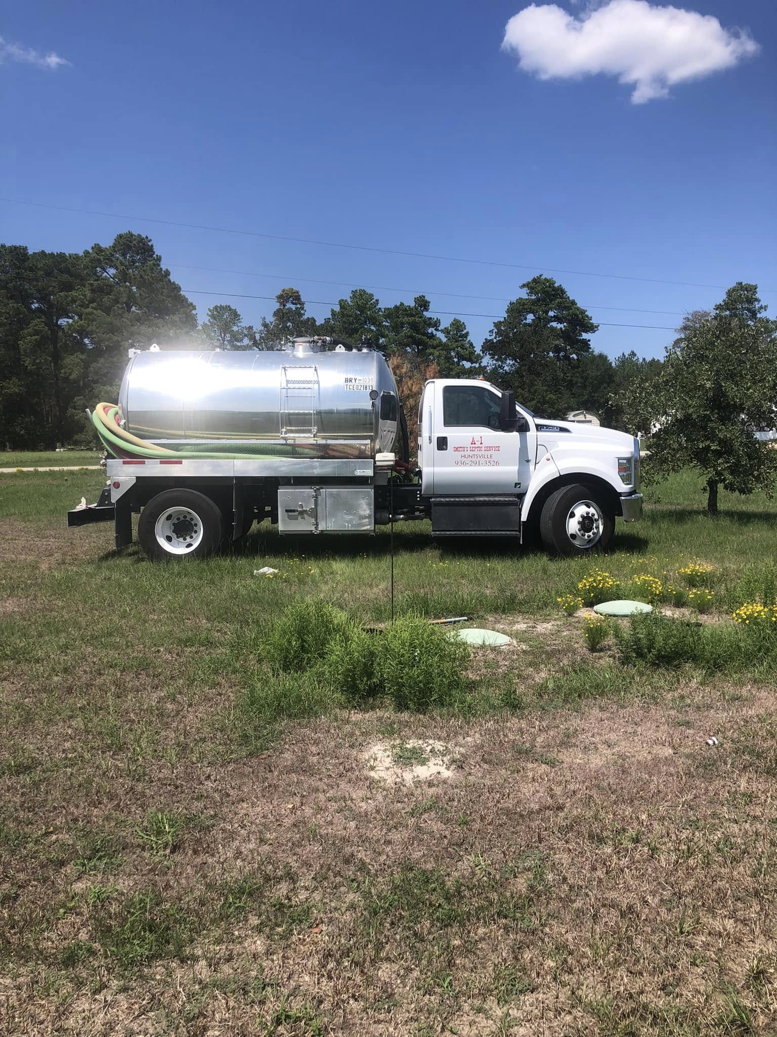 A-1 Smith's septic pump truck with green and red vacuum hoses servicing rural property with visible septic tank access lids in Huntsville TX area