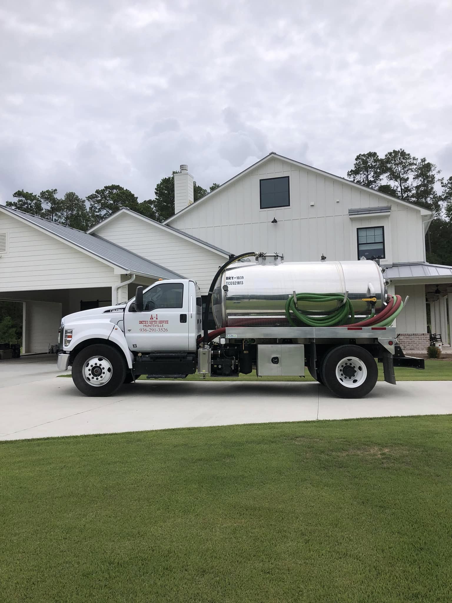 A-1 Smith's white Ford septic vacuum truck with stainless steel tank servicing a modern residential home with manicured lawn in East Texas
