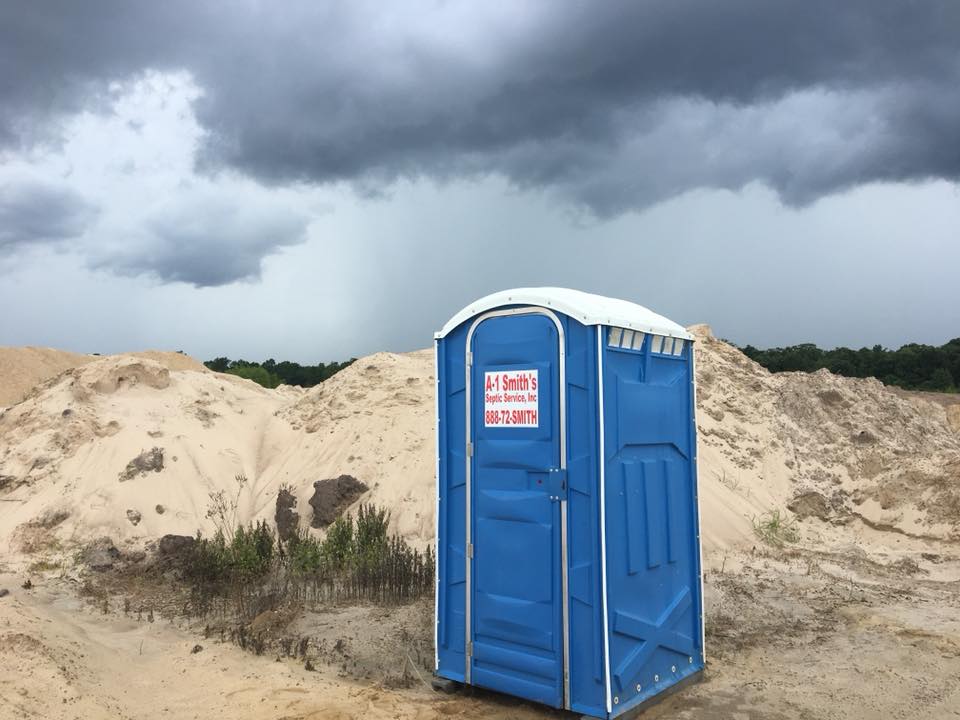 A-1 Smith's Septic Service portable toilet at construction job site with sand piles and dramatic Texas sky showing 888-72-SMITH phone number