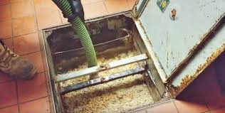 Professional grease trap pumping service - technician cleaning commercial kitchen grease trap with vacuum hose removing accumulated fats oils and grease FOG in Huntsville TX